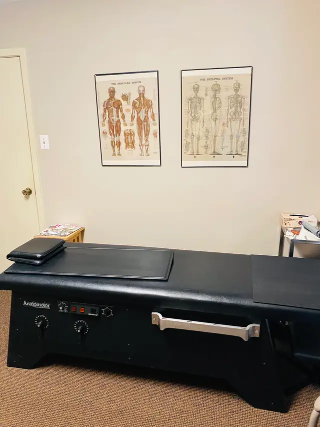 Treatment room at Tyler Chiropractic: a black Anatomotor table under framed muscular and skeletal system charts